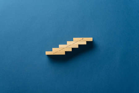 Wooden pegs placed in a stairway like structure with a rising arrow drawn on it. Over blue background with plenty of copy space.の写真素材