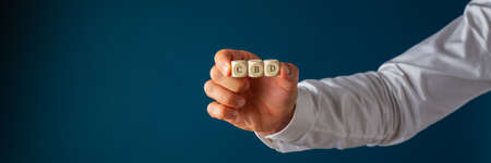 Wide view image of male hand holding wooden dices reading CBD in his hand. Over blue background.の写真素材