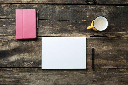 Top view of digital tablet in pink cover, blank white sheet of paper, black pen and a cup of fresh coffee placed on rustic wooden desk.の写真素材