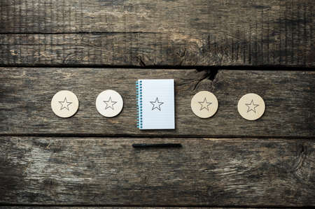 Five stars drawn on wooden cut circles and notepad, with black pen lying around. Over rustic wooden background.の写真素材
