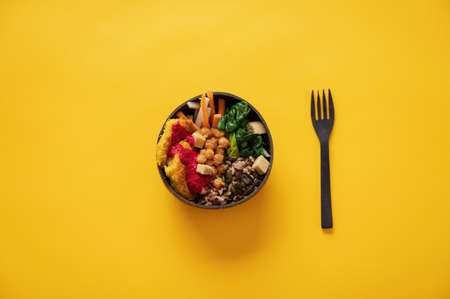 Top view of delicious vegan meal serve in buddha bowl with a coconut fork next to it. Over yellow...