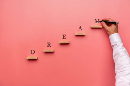 Businessman writing the word Dream above wooden pegs placed in stairway like structure.の写真素材
