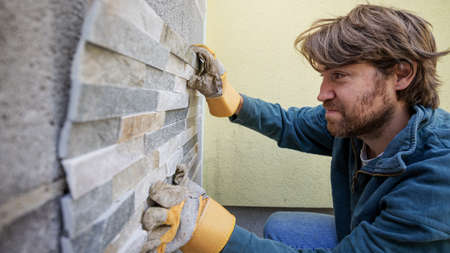 Young man laying ornamental tiles on an outside wall.