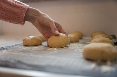 Female hand placing sourdough balls on a floured surface on kitchen counter.