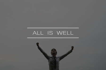All is well sign above a content young businessman standing with his arms raised high under cloudy sky. の写真素材