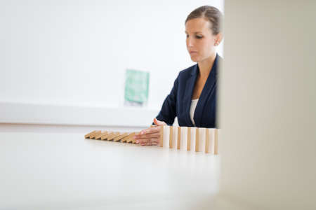 Serious young businesswoman stopping falling dominos with her hand in a conceptual image of business crisis management. の写真素材