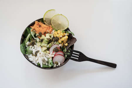 Top view of mixed vegan salad with carrots, radishes, corn and avocado served in coconut buddha bowl. Over white background.の写真素材