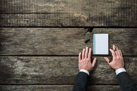 Top view of a businessman about to write in a blank notepad with black marker. Over rustic wooden background with plenty of copy space on the left side of an image.の写真素材