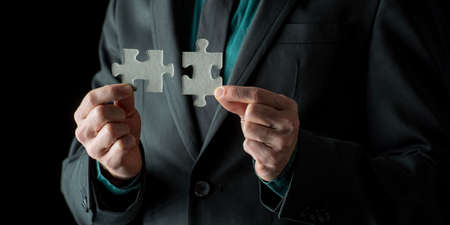 Closeup view of businessman putting together two blank matching puzzle pieces.