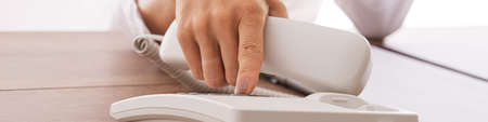 Wide view closeup image of a secretary dialing telephone number on white landline phone.の写真素材