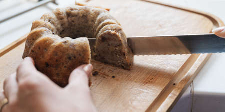 Closeup view of female hand cutting freshly baked vegan banana bread with chocolate and pecans.の写真素材