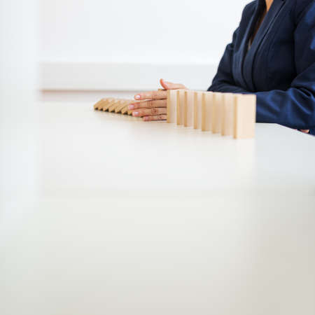 Low angle view of businesswoman stopping collapsing dominos with her hand in a conceptual image of...