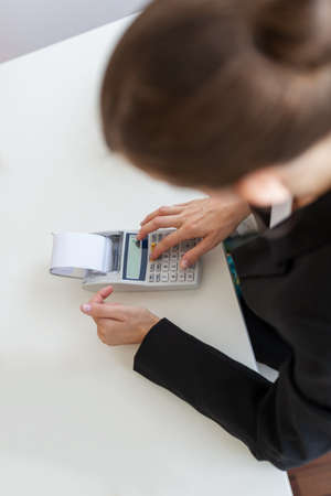 View from above of a female business accountant using calculator while working at her office desk.