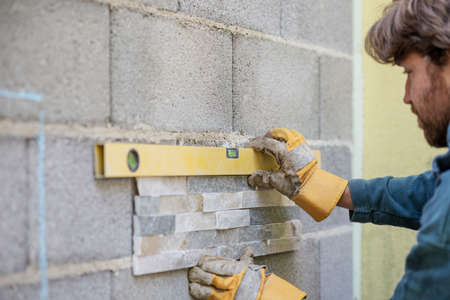 Young man using a yellow label against a wall while placing an ornamental tile in a home diy project.の写真素材