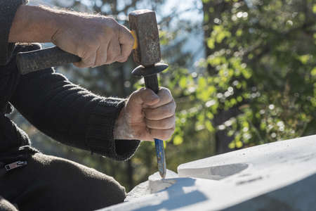 Low angle closeup view of an artist carving precise curves in white stone using chisel and mallet.