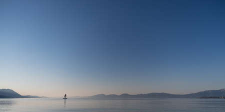 Beautiful calm nature of morning sea with one woman paddling on sup board in the distance.