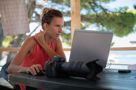Young female photographer editing phots on her laptop computer while on vacation in summer beach...