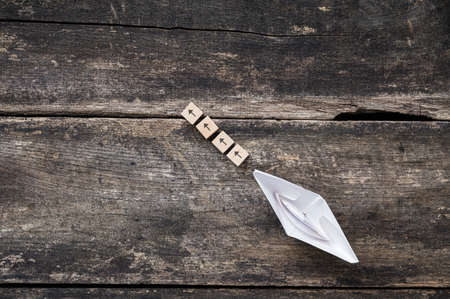 Wooden blocks with arrow symbols on them leading direction to a paper made origami boat in a conceptual image of business vision and direction.の写真素材