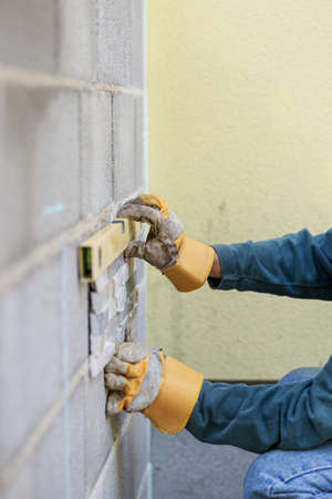 Male hand in protective work gloves using yellow label to position an ornamental tile on build wall...