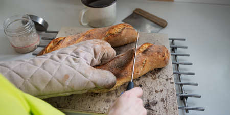 Over the shoulder view of of woman wearing kitchen mitten cutting hot freshly baked home made...