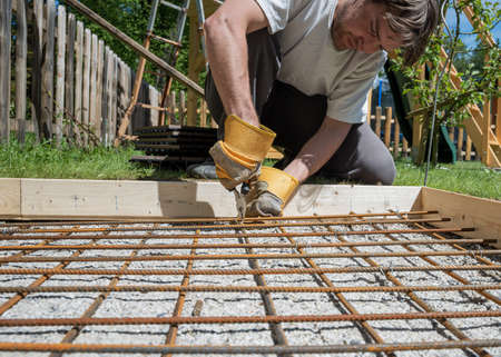 Low angle view of a man making a net of steel bars by clipping them together with a wire and pliers...