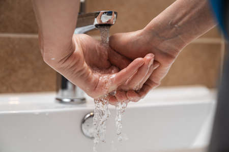 Closeup view of a woman thoroughly washing her hands with clean tap water in home bathroom.の写真素材