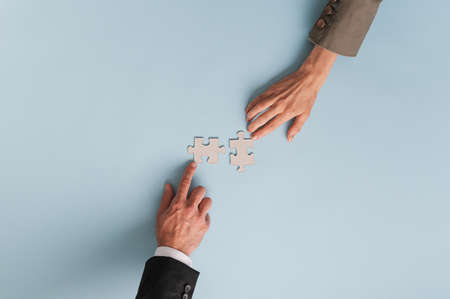 Top view of hands of businesswoman and businessman joining two blank matching puzzle pieces. Over blue background with copy space.の写真素材