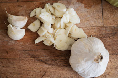 Top view of garlic bulb next to chopped garlic cloves on wooden cutting board. 