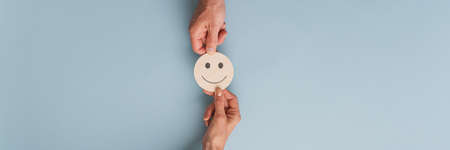 Male and female hands holding wooden cut circle with smiling face on it. Over blue background with copy space.の写真素材