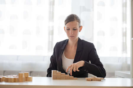 Young businesswoman sitting at her office desk walking her fingers up the steps made of wooden pegs...