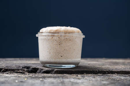 Low angle view of heaping jar of sourdough starter yeast placed on rustic wooden board over blue background.の写真素材