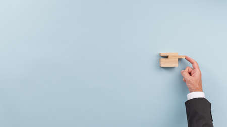 Hand of a businessman pushing a wooden peg in stack of them in a conceptual image of business start up. Over blue background.の写真素材