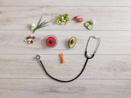 Healthy eating and care for ones health conceptual image - smiling face made of stethoscope, raw veggies, avocado and vegan dip.の写真素材