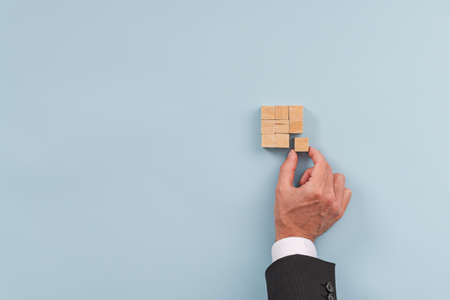 Hand of a businessman building a squared structure of wooden blocks in a conceptual image of...