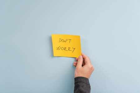 Male hand placing yellow post paper with a Dont worry sign over light blue background.の写真素材