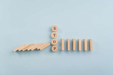 Word stop spelled on wooden cut circle interrupting falling dominos in a conceptual image. Over blue background.の写真素材