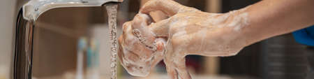 Wide closeup view of a woman washing her hands thoroughly with soap foam at home in bathroom.