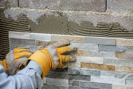 Pressing ornamental tile in the look of a natural stone into an adhesive glue on a wall in backyard.の写真素材