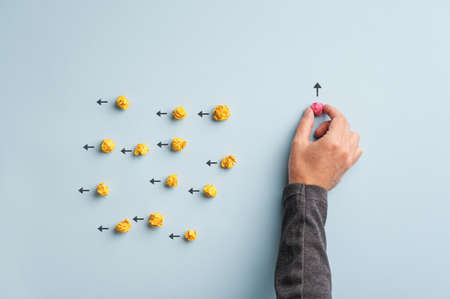 Male hand taking a smashed pink ball of paper out of a group of others, yellow ones, in a conceptual image od individuality.の写真素材