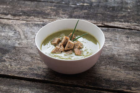 Delicious creamed broccoli soup with home made bread croutons placed on rustic wooden desks. の写真素材