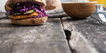 Low angle view of delicious vegan burger made of chickpea topped with zucchini, red cabbage and dressing in home made sourdough bread bun.の写真素材