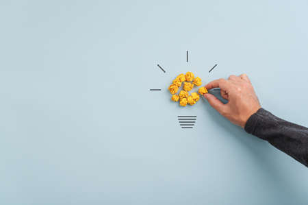 Male hand making a light bulb of smashed yellow papers in a conceptual image of idea and creativity.の写真素材