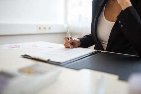 Closeup view of businesswoman sitting at her desk signing a document or contract in a folder.