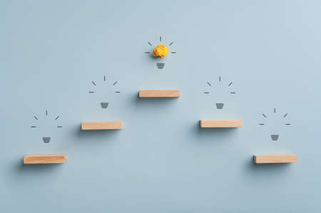 Innovation and realization conceptual image - pyramid shaped staircase leading to the topo glowing light bulb. Over blue background.の写真素材