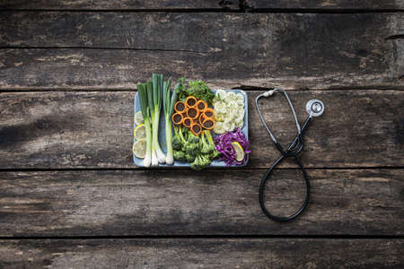 Healthy eating and diet - plate full of fresh vegetables next to a stethoscope placed on rustic...