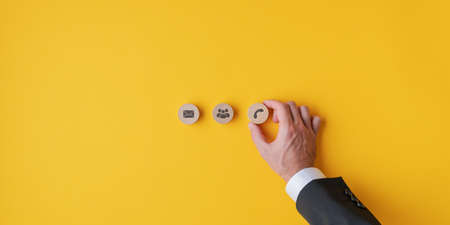 Hand of a businessman placing three wooden cut circles with contact and communication icons and symbols on them over yellow background.の写真素材