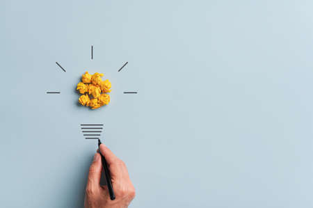 Male hand making a light bulb with smashed yellow papers in a conceptual image of vision and innovation.の写真素材