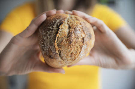 Closeup view of a woman holding freshly baked homemade bread bun showing it to the camera.の写真素材