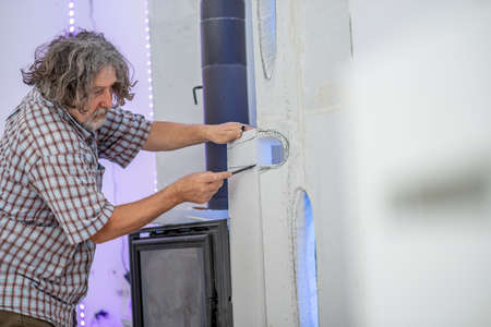 Senior man carving in a wall to create beautiful ornamental forms around a fireplace in a home.