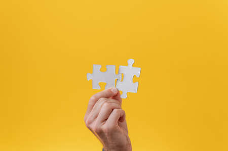Male hand holding two matching puzzle pieces in his hand in a conceptual image. Over yellow...